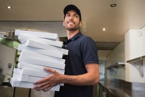 Smiling pizza delivery man holding many pizza boxes in a commercial kitchen